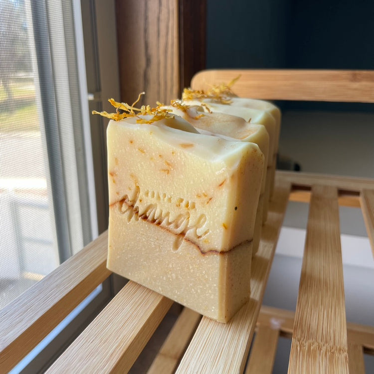 Handmade soaps sitting upright on a wooden shelf. The soaps are layered with yellow and white soap layers, with dried yellow flower petals on the top.